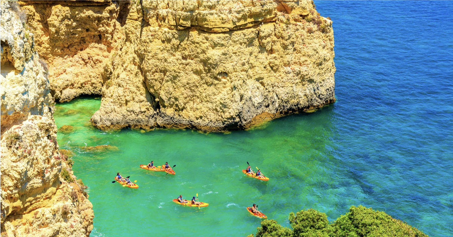 Kayakers exploring clear turquoise water beneath Algarve cliffs